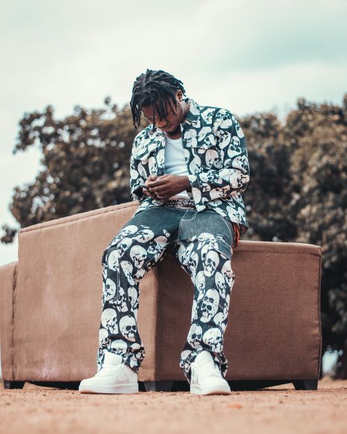 Free Young man wearing skull patterned clothes sitting outside on a sofa, relaxed and stylish. Stock Photo