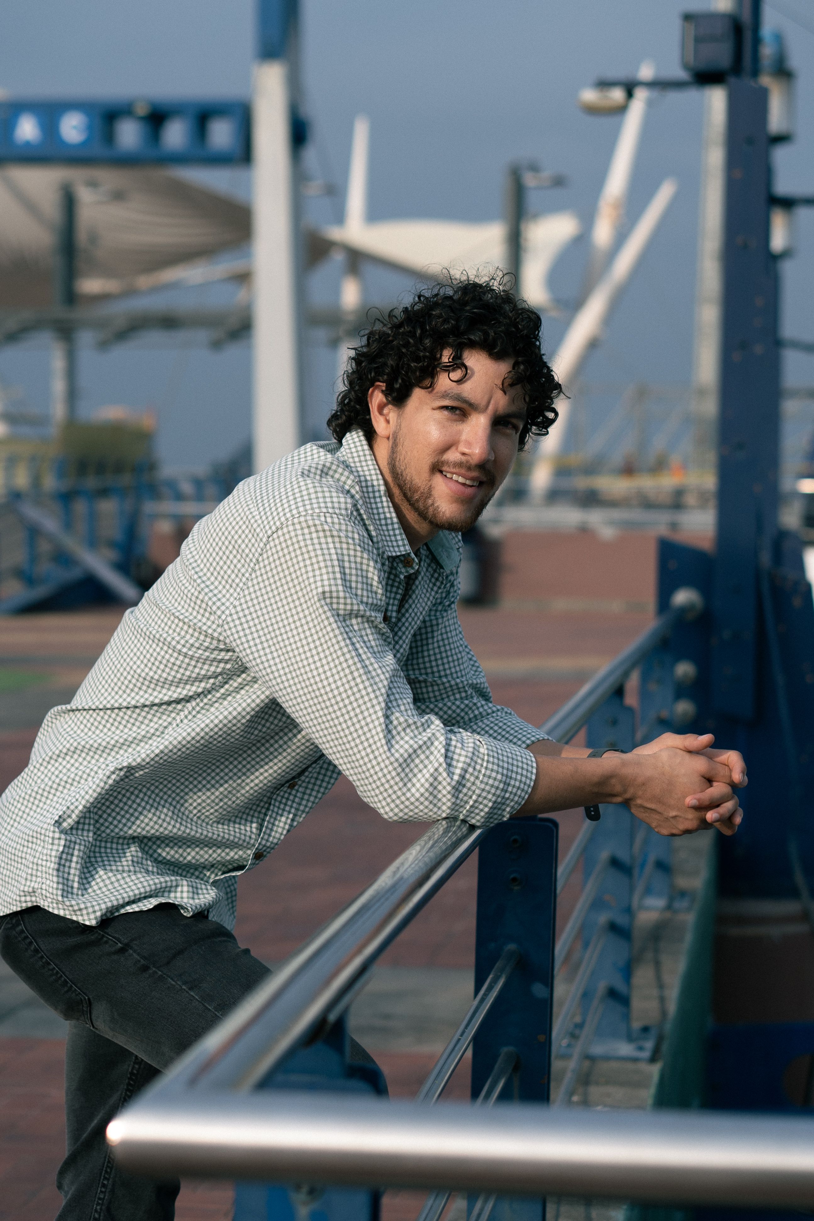 A man in a shirt and jeans leaning against a railing · Free Stock Photo