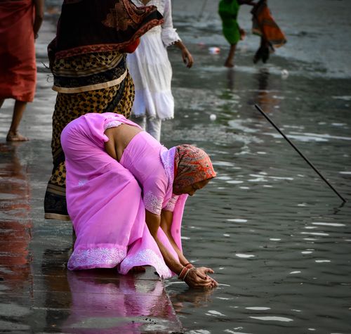 Free A woman in vibrant traditional clothing participates in a riverside ritual, adding cultural depth to the scene. Stock Photo