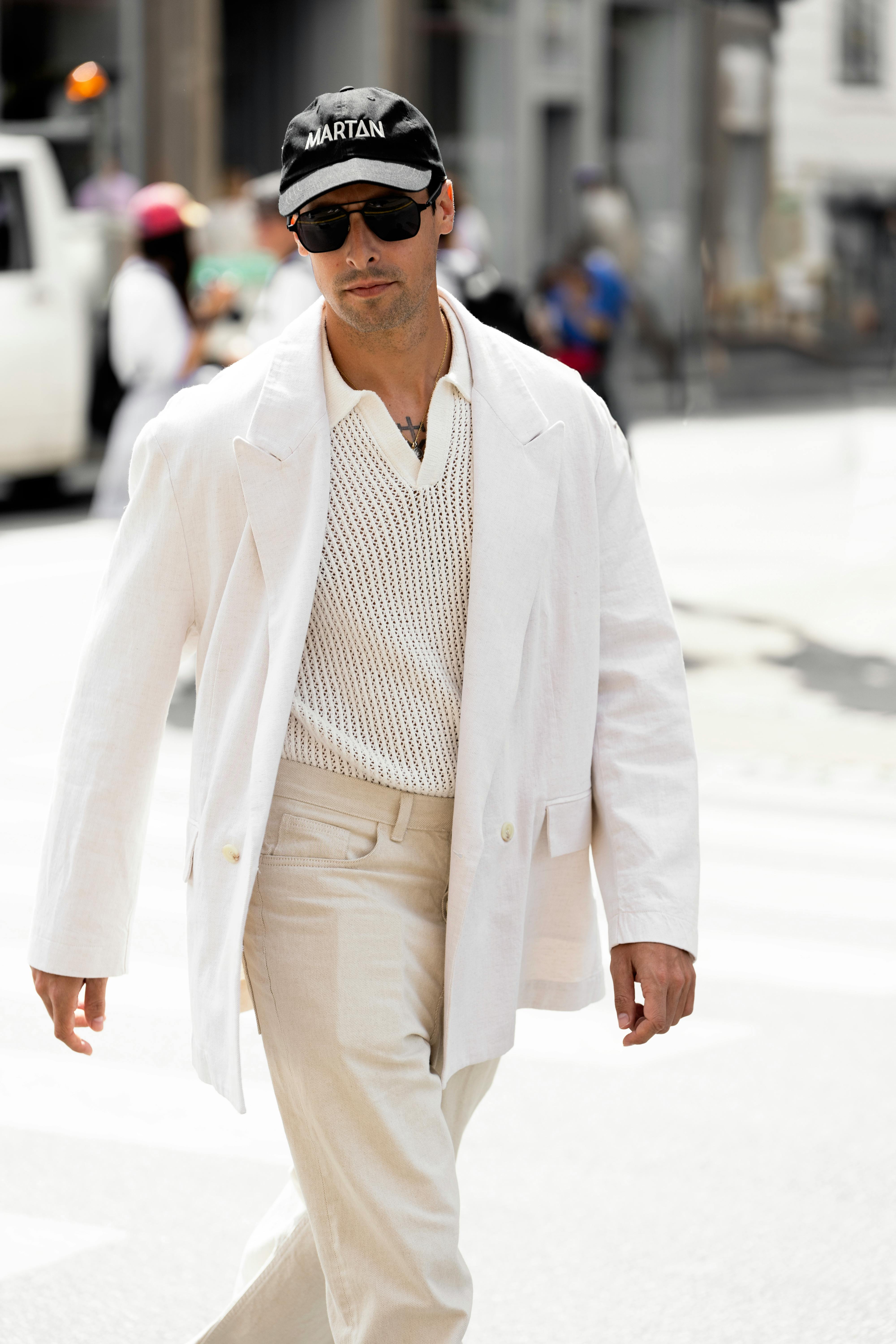 Confident man in white suit and sunglasses walking in a bright city street.