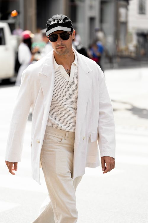 Free Confident man in white suit and sunglasses walking in a bright city street. Stock Photo