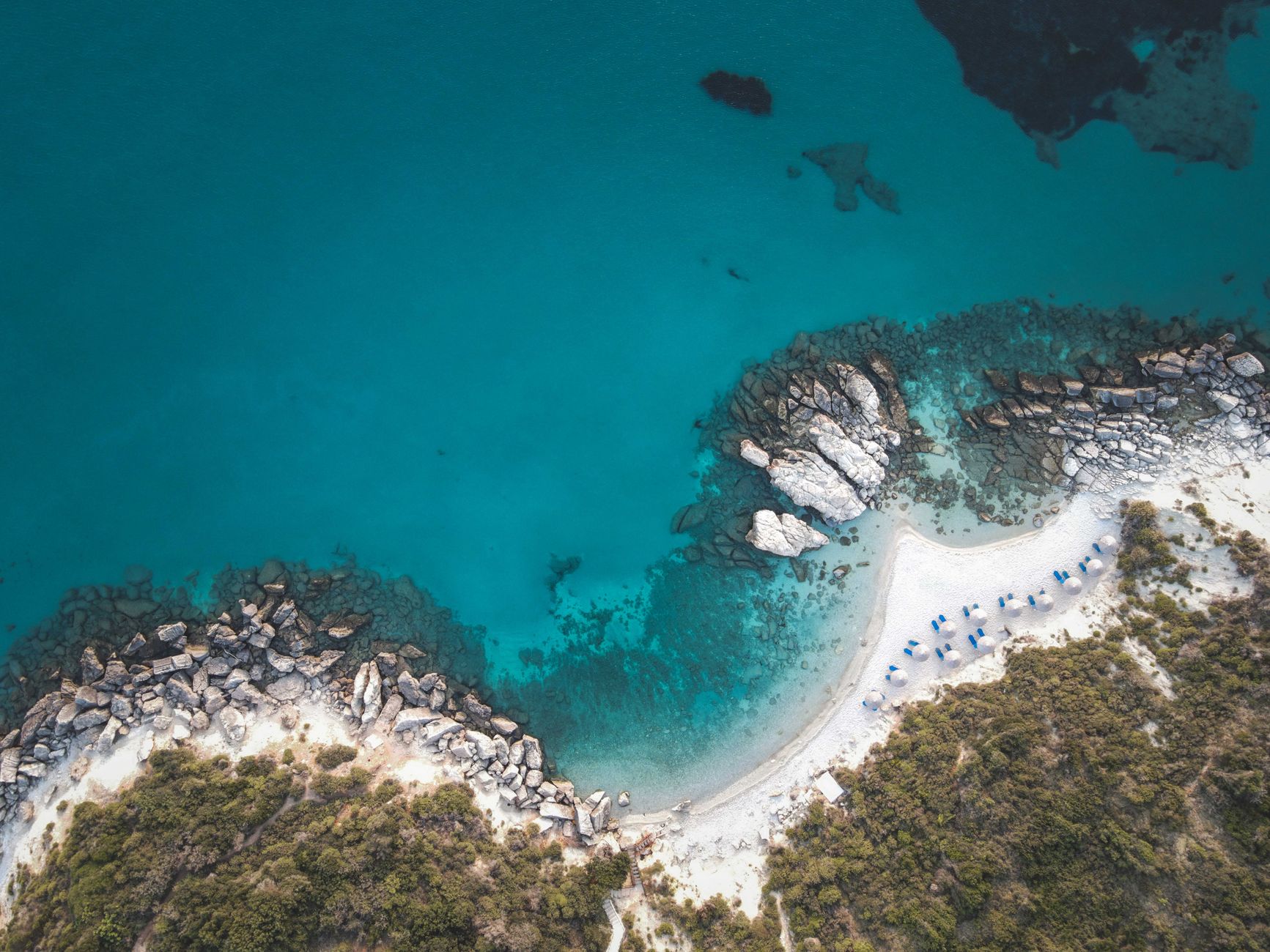 A breathtaking aerial view of a picturesque turquoise beach cove with white sand and lush greenery.