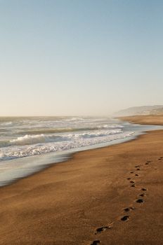 Footprints in sand along the tranquil beach in Lincoln City, OR at sunset.