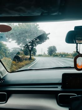 View from inside a car driving on a winding countryside road. Lush greenery and cloudy skies outside.