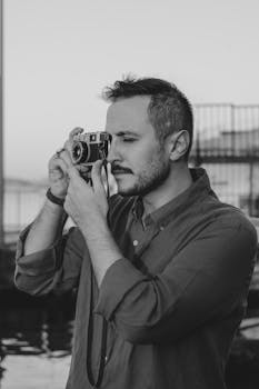 Artistic black and white portrait of a man using a vintage camera outdoors.
