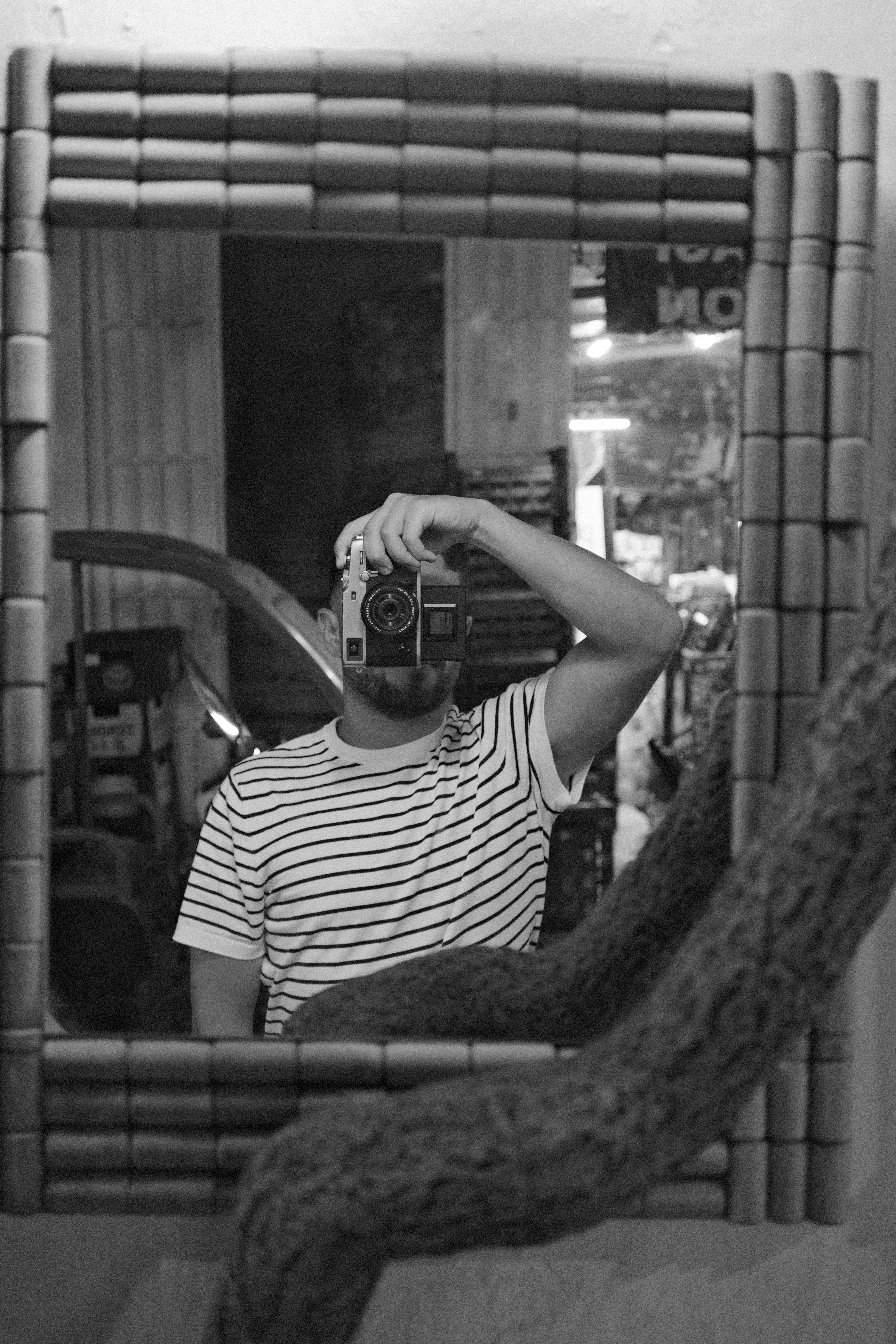 A man captures a mirror selfie using a vintage camera indoors in monochrome.
