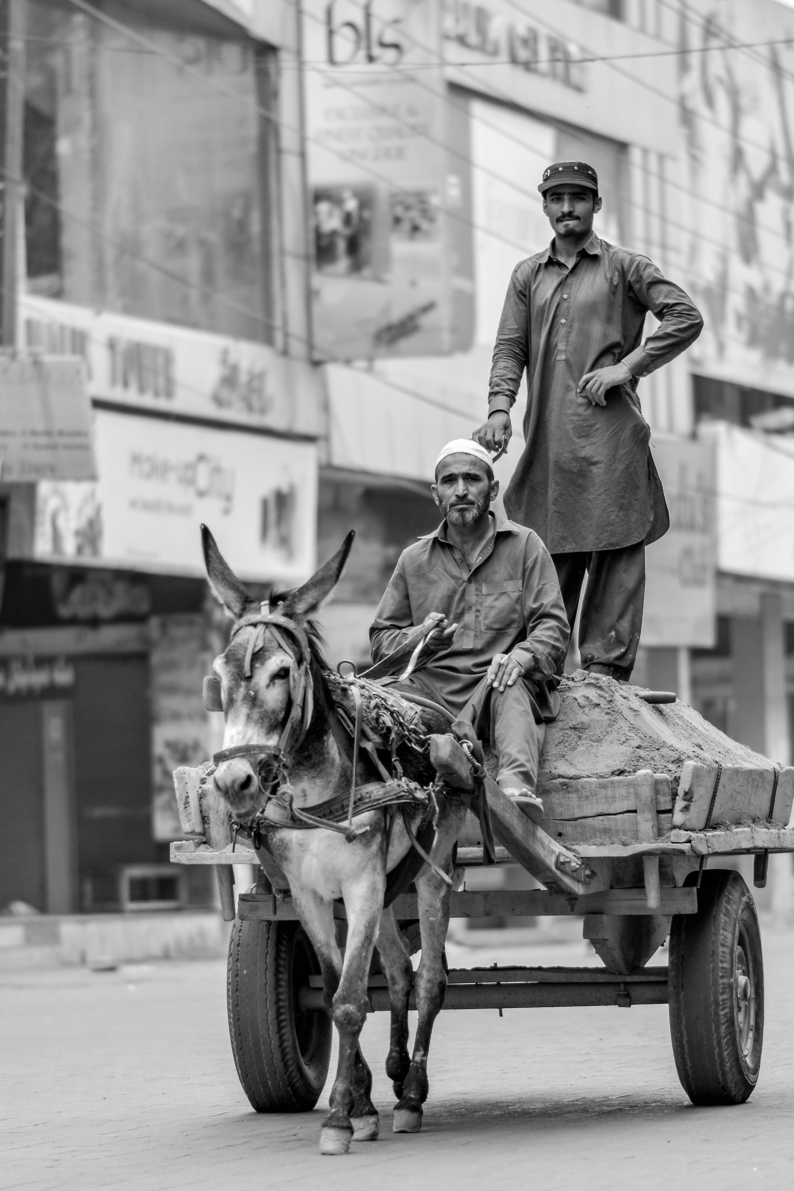 Two men ride a donkey cart through a busy urban street, showcasing traditional transportation methods.