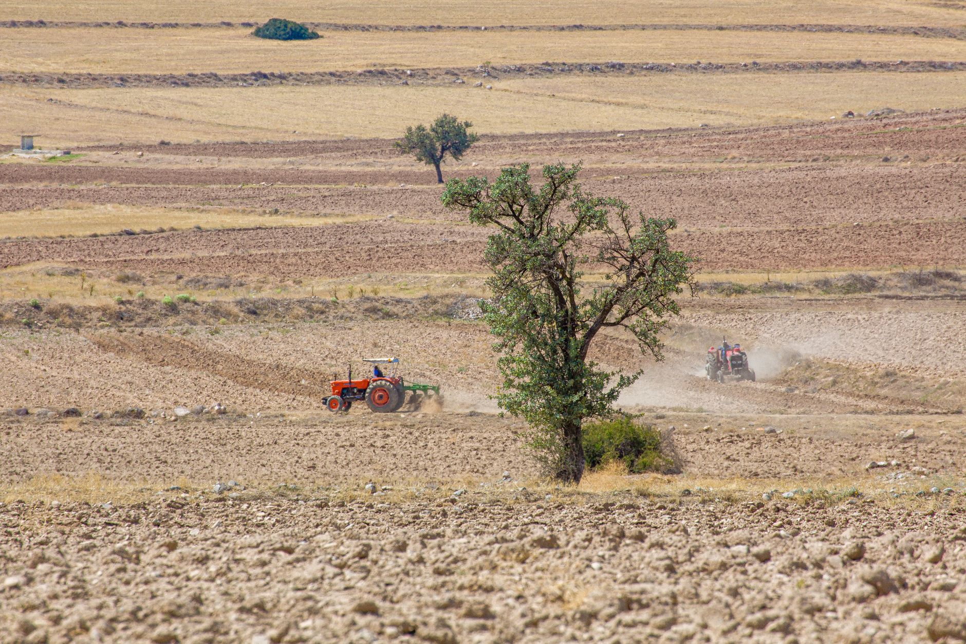 Suha zemlja i traktor u polju pod jakim suncem