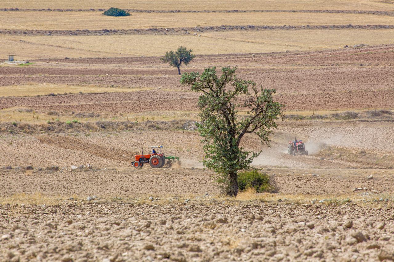 Suha zemlja i traktor u polju pod jakim suncem