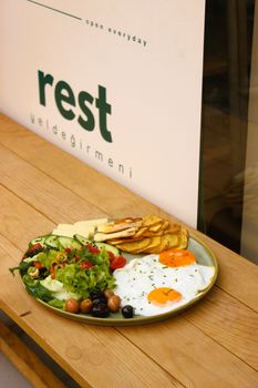 A vibrant breakfast spread featuring eggs, salad, pancakes, and cheese on a wooden table.