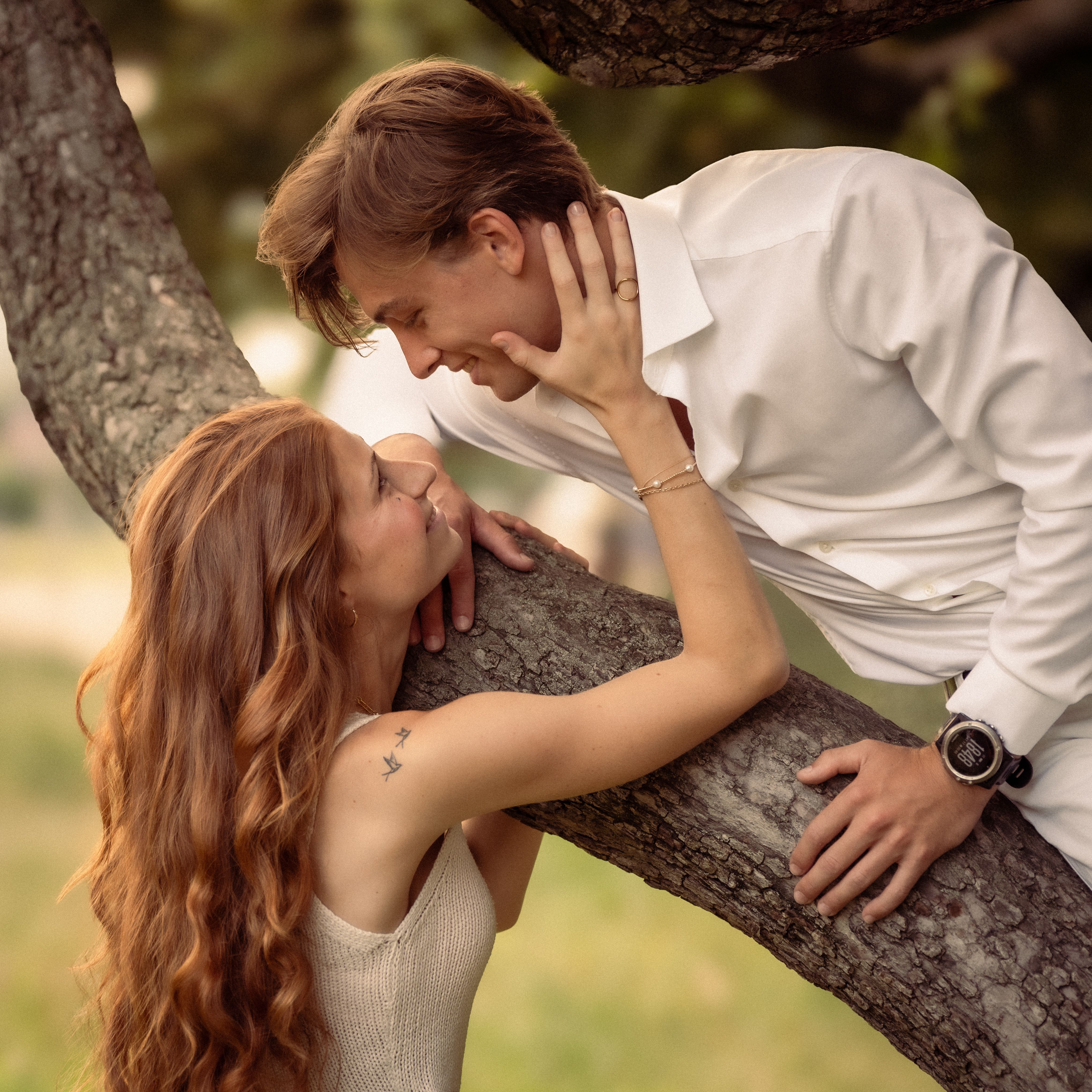 Young couple sharing a romantic moment by a tree in a sunny park, capturing love and connection.