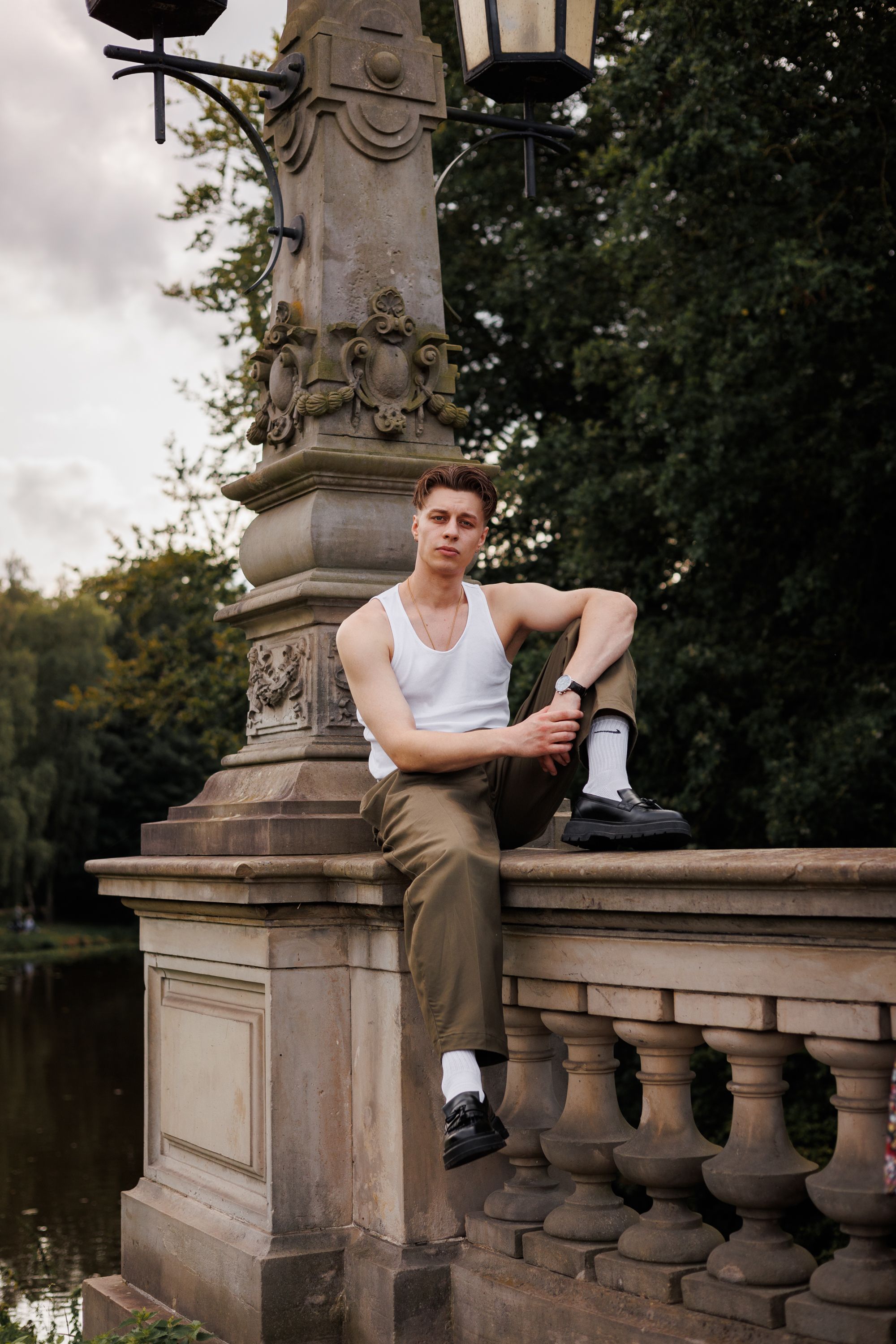 Casual portrait of a young man sitting on a decorative stone railing by a canal.