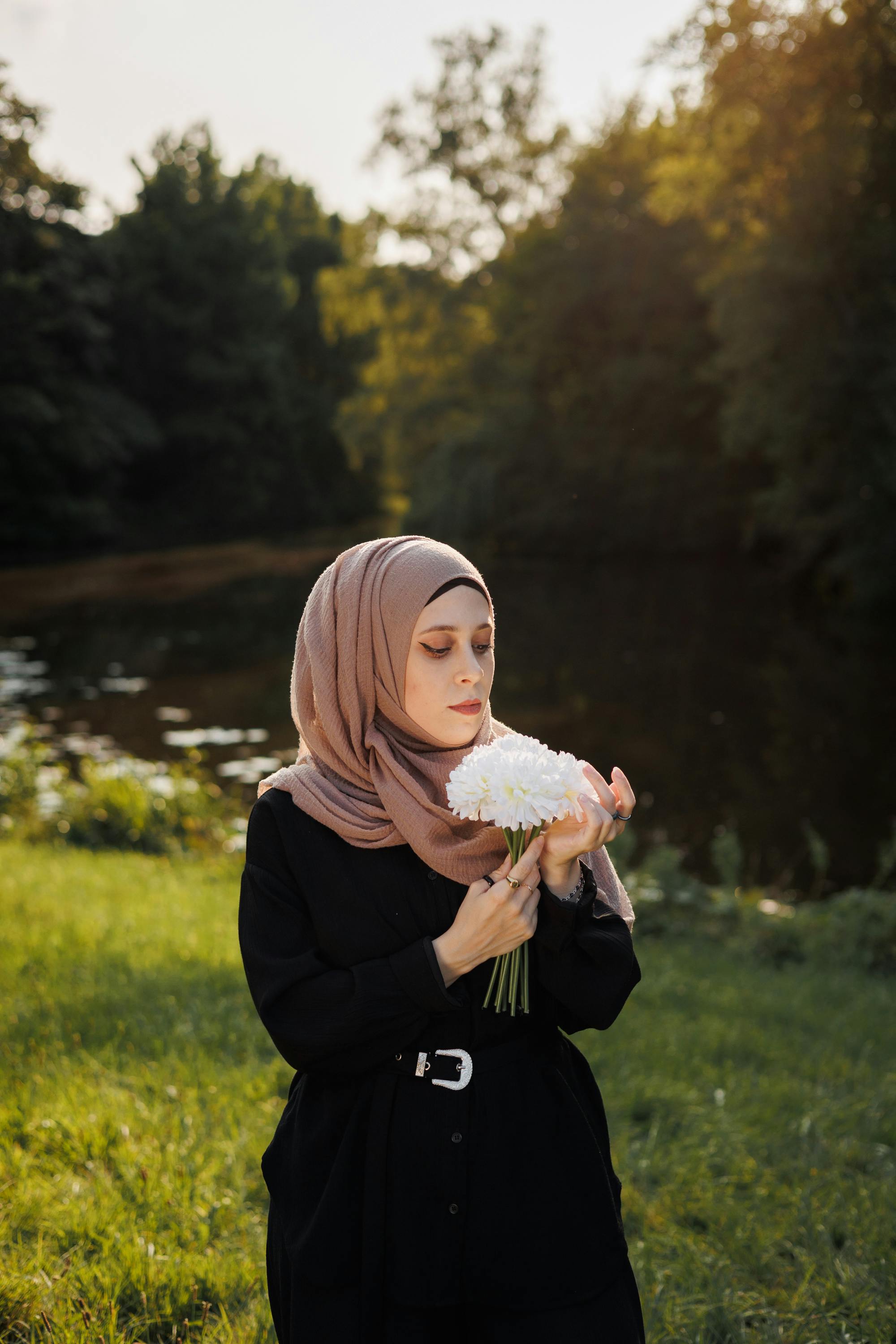 A woman enjoying a peaceful moment holding flowers by the lakeside during sunset.
