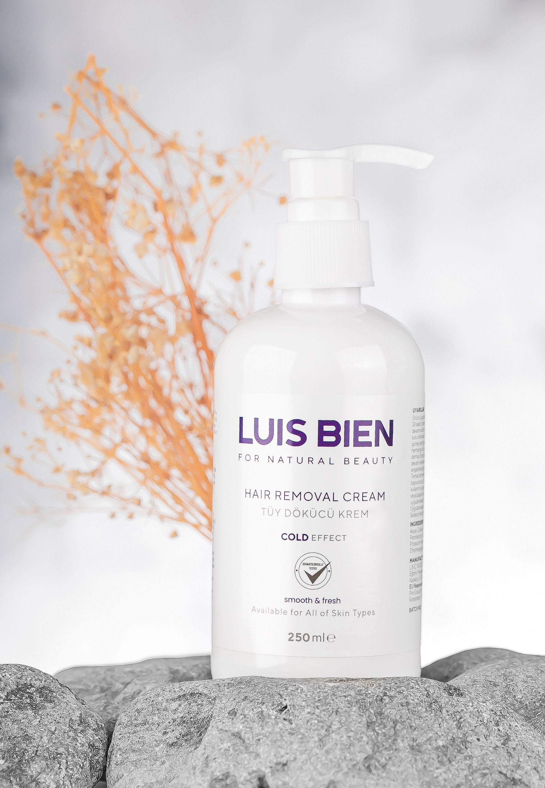 A white bottle of hair removal cream sits on stones with dry branches in the background.