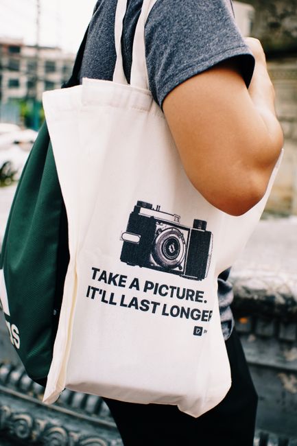 Close-up of a tote bag with a camera print and motivational quote, perfect for photography enthusiasts.