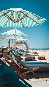 A relaxing sunny beach scene with lounge chairs and striped umbrellas by the ocean.