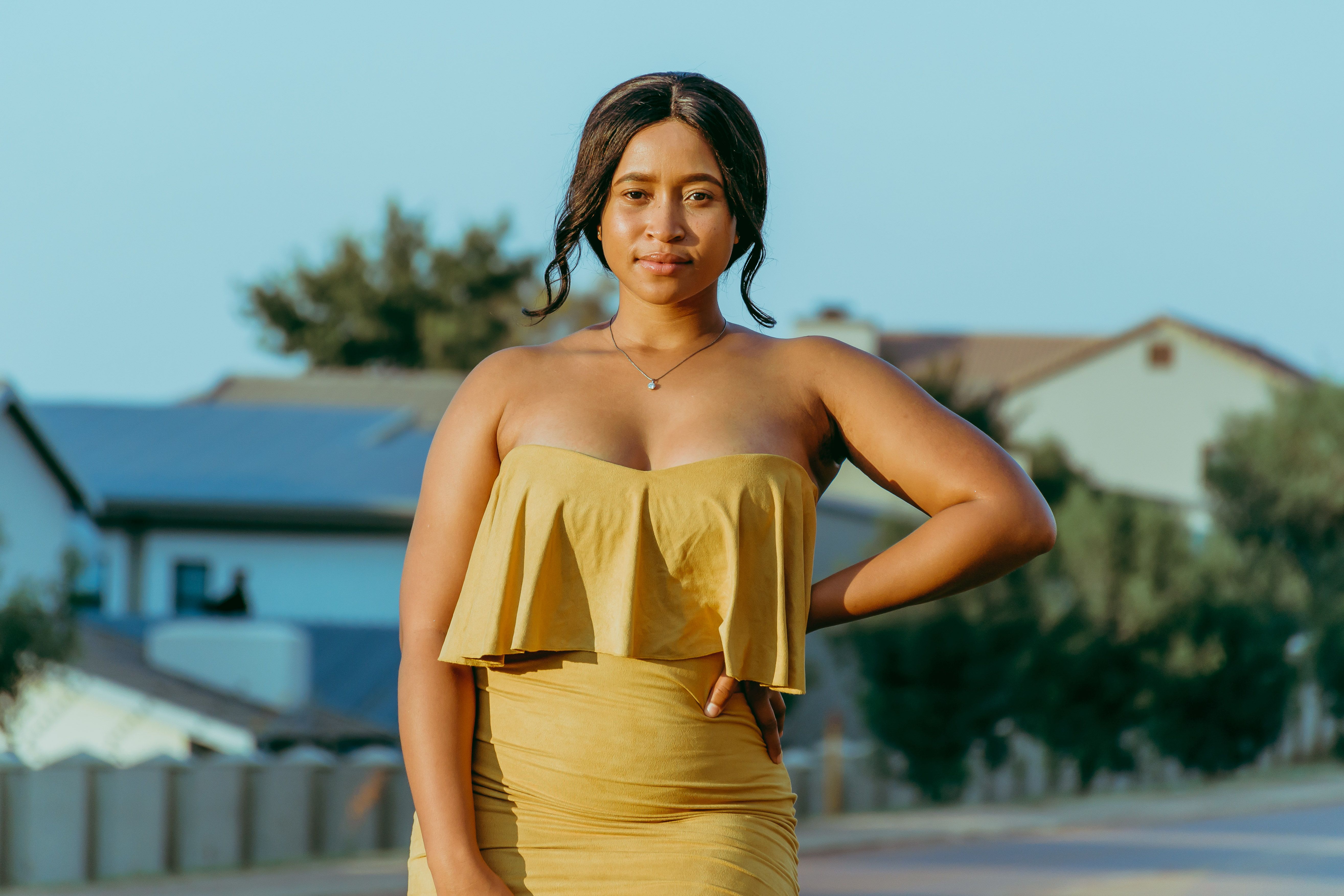 Charming outdoor portrait of young woman in yellow dress, sunny day.