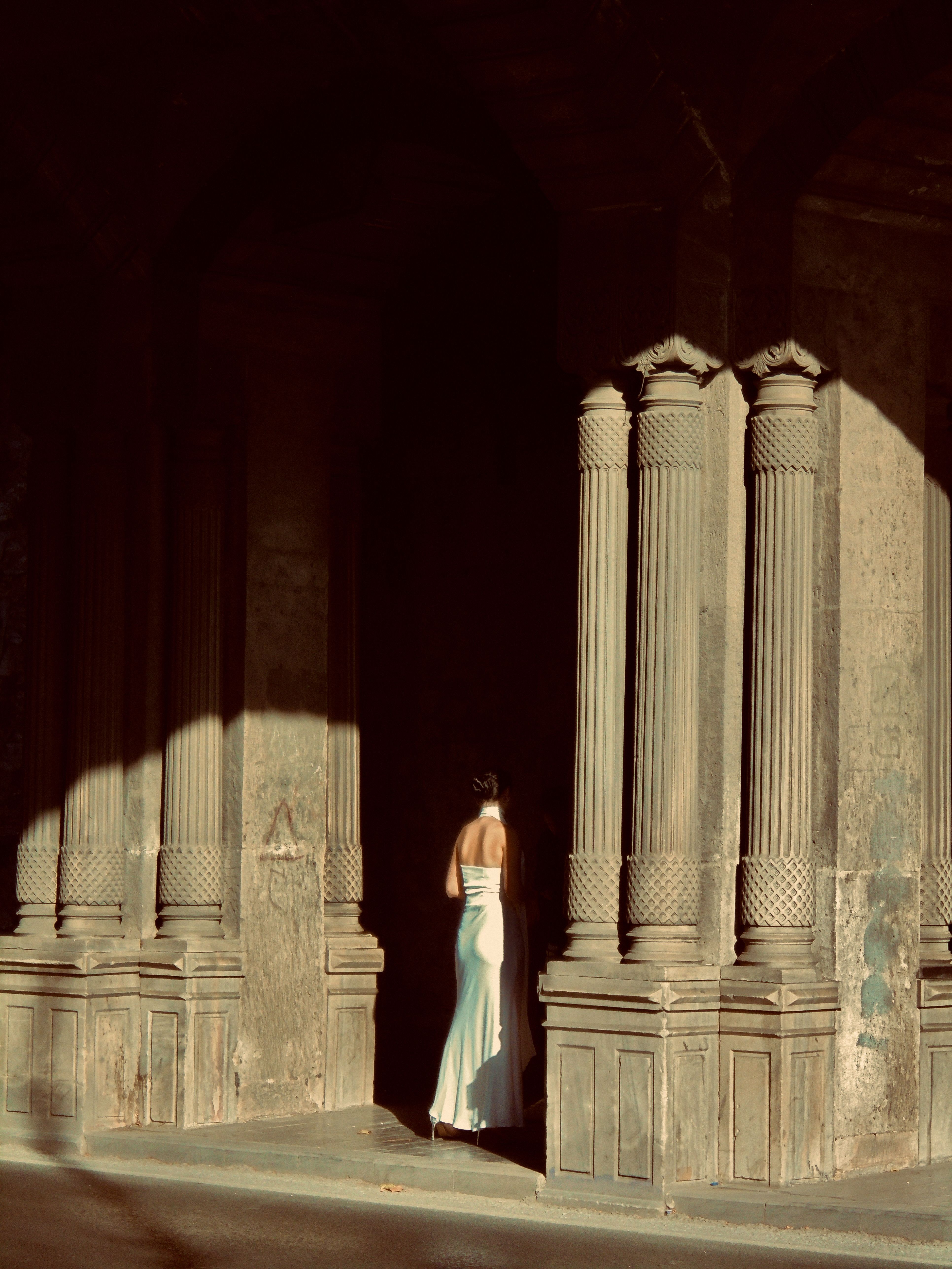 A woman in a white dress standing in front of pillars · Free Stock Photo