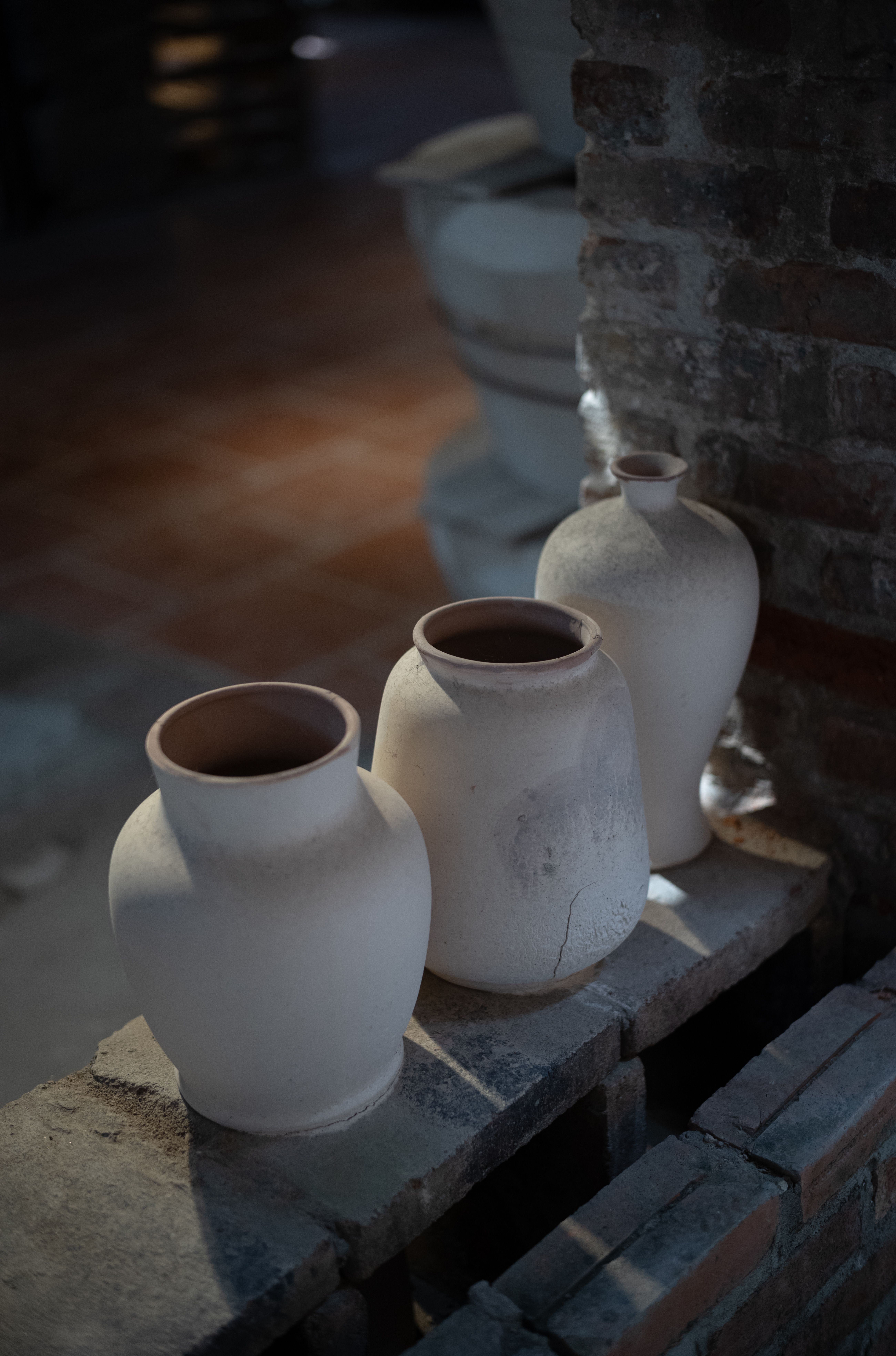 Three pit-fired clay vessels by Marisol Quintana resting on a brick ledge in soft shadow