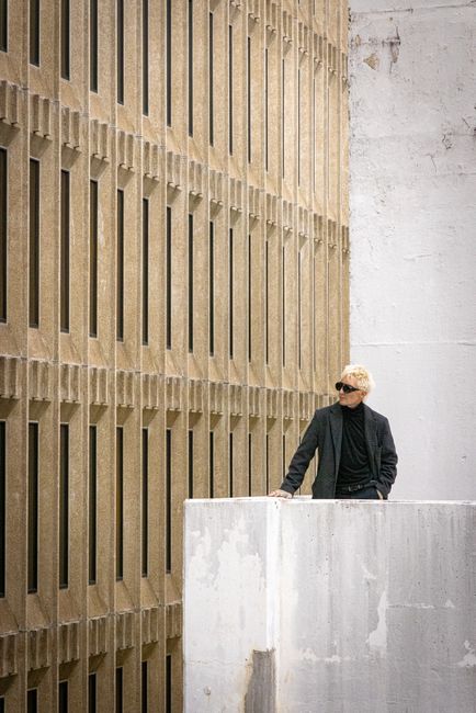 A stylish man stands near a modern building, exuding urban elegance.