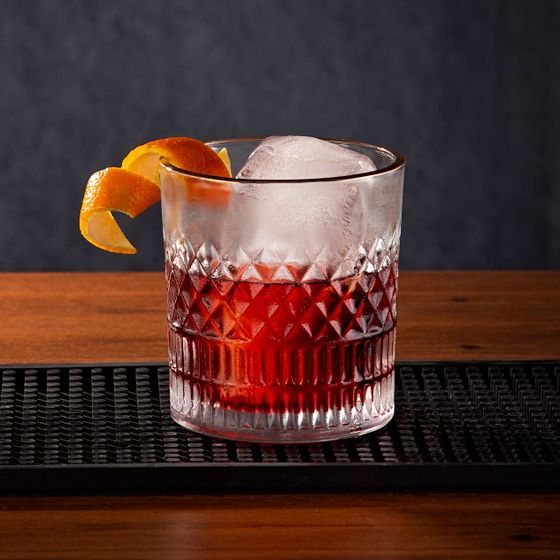 Deep red negroni in a cut crystal glass with a large ice cube and orange peel