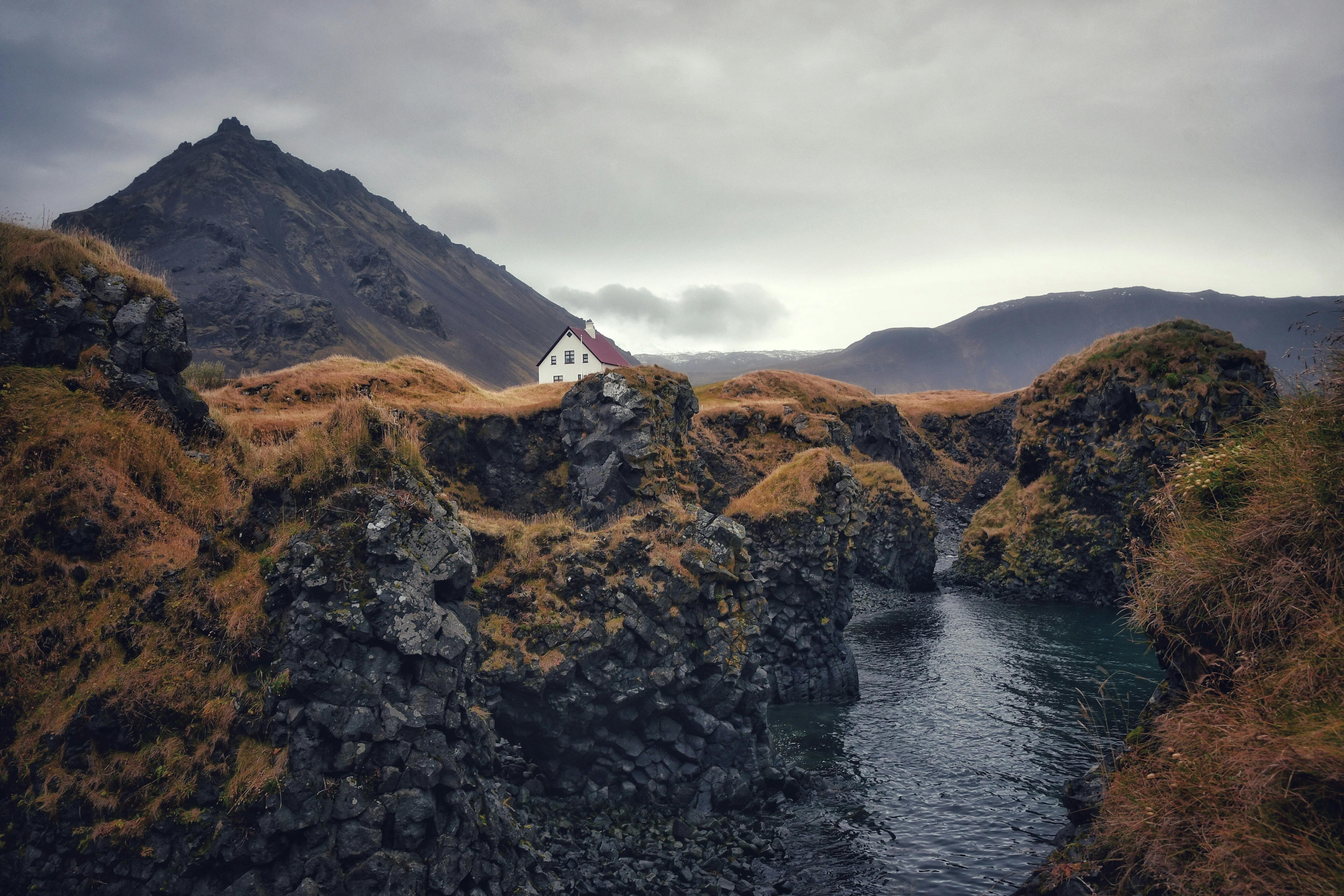 A picturesque remote house nestled among rugged mountains and a tranquil stream.