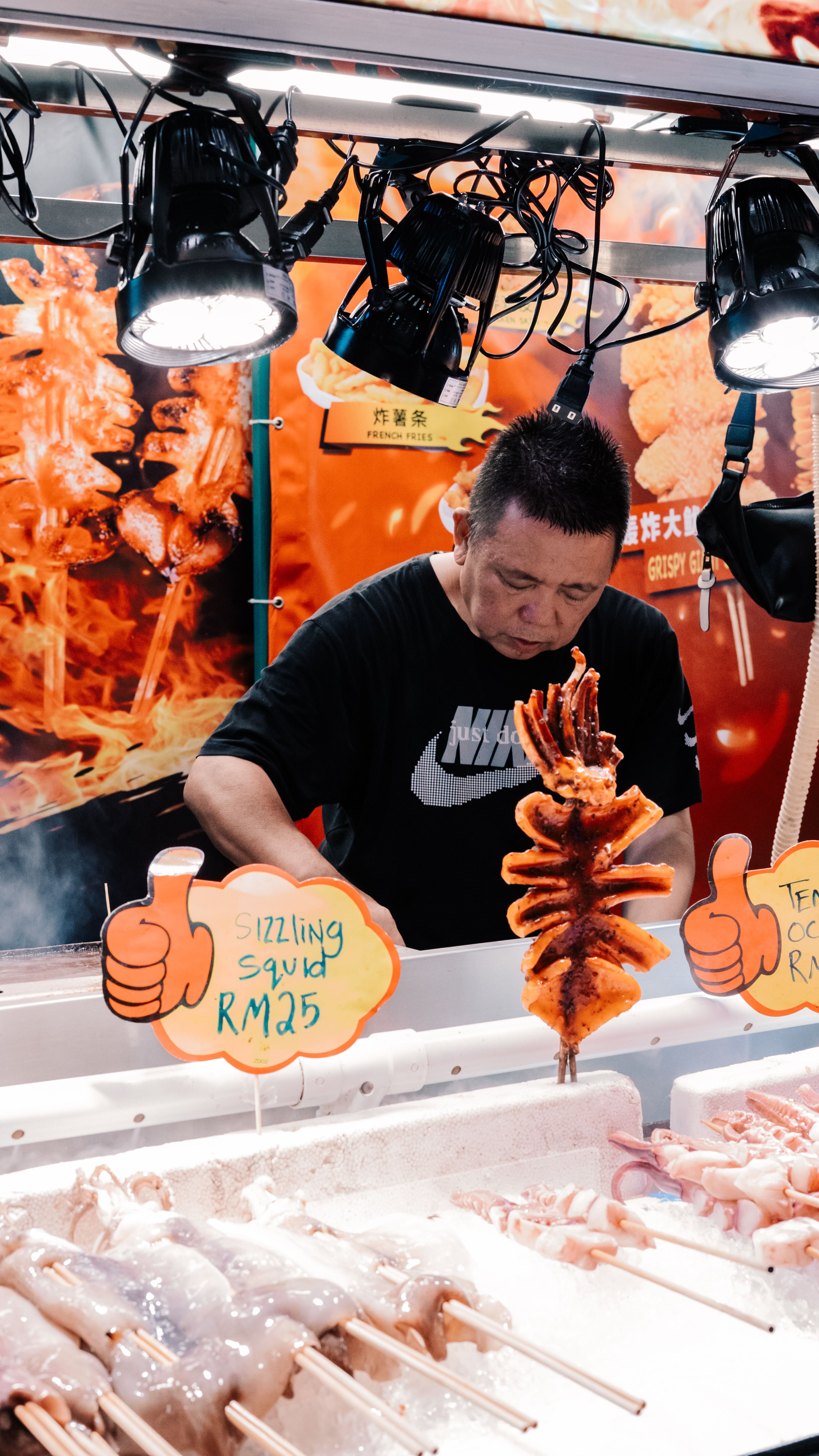 A street vendor cooking sizzling grilled squid at a bustling seafood market.