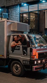 A happy truck driver gives a thumbs-up while parked in a city street at night.