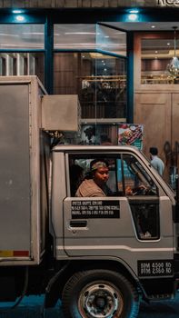 Driver in a truck cab on a city street at night, showcasing urban life.