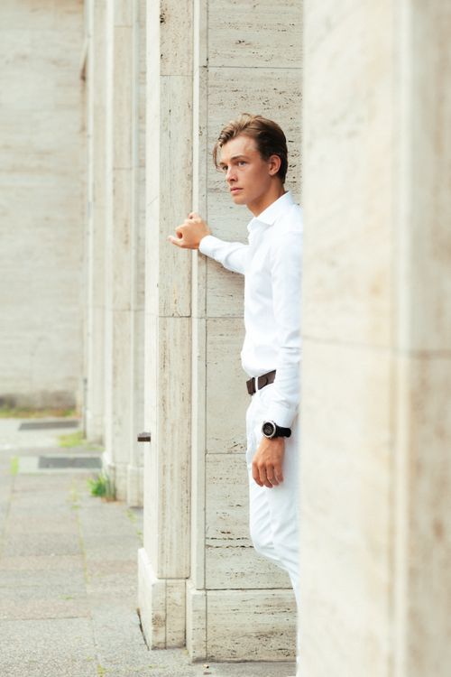 Free A young man in white clothing stands confidently in a modern architectural setting in Berlin. Stock Photo