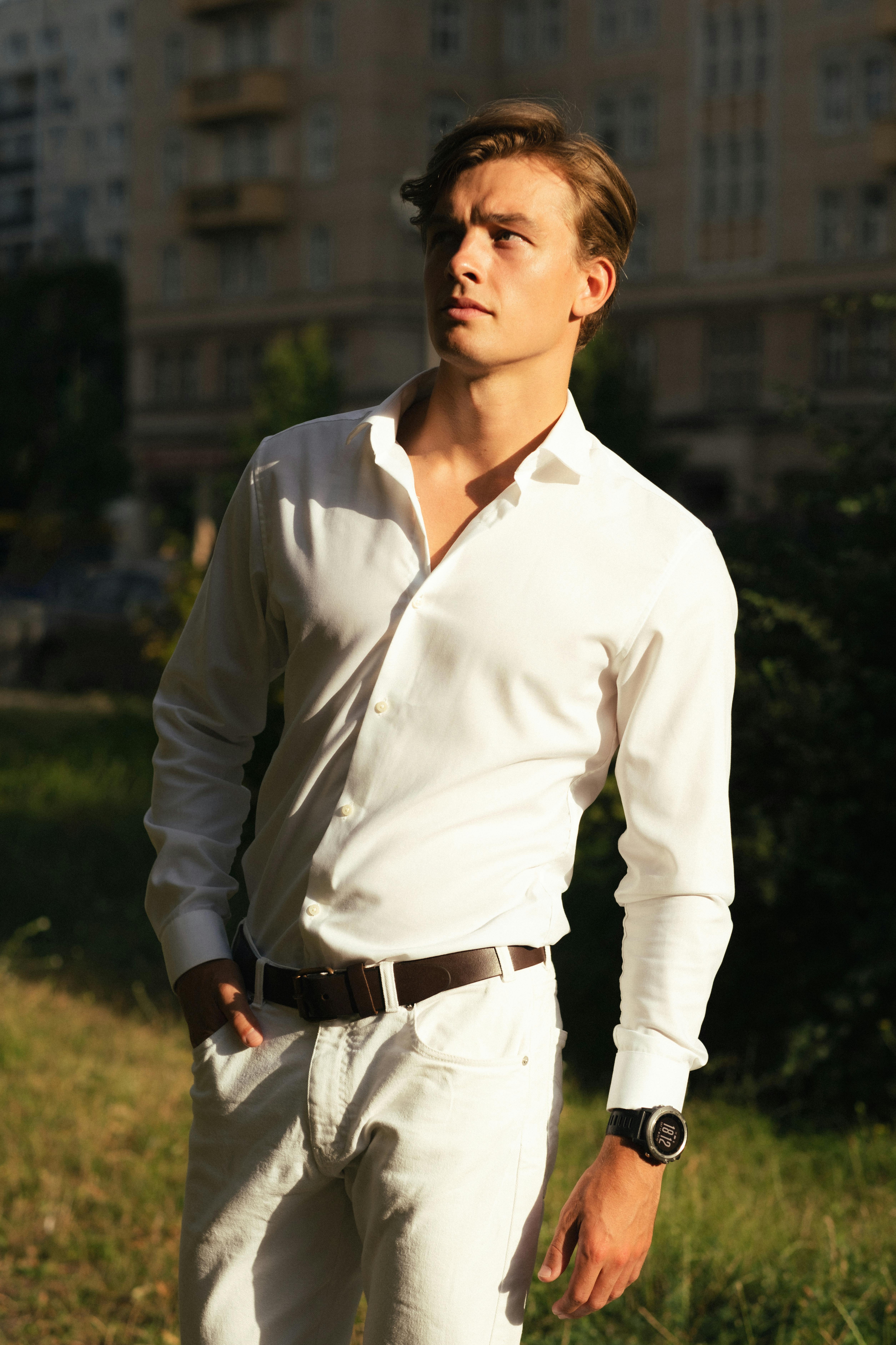 Elegant portrait of a man in a white outfit with sunglasses in Berlin's urban setting.