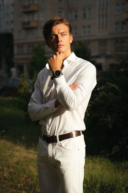 Portrait of a young man in a white outfit, posing confidently outdoors during daylight in Berlin.