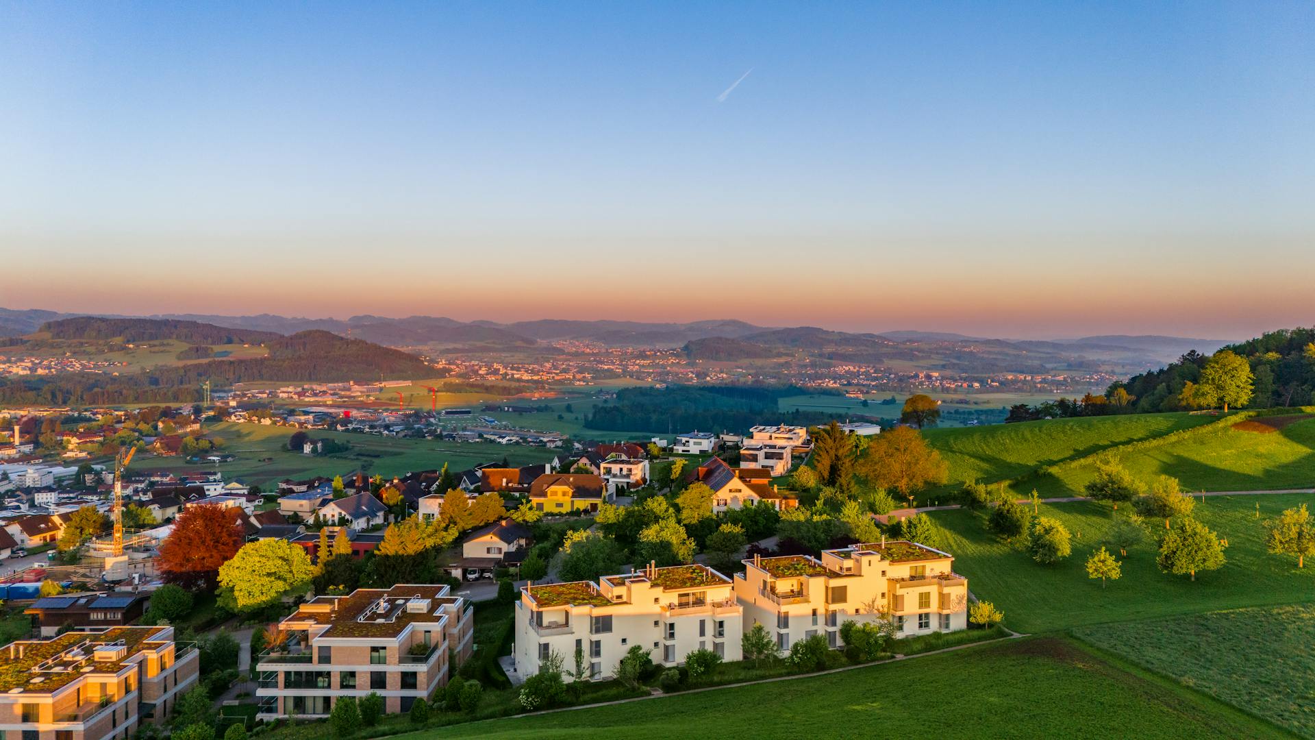 Stunning aerial view of idyllic Swiss town in summer with rolling hills and clear skies.