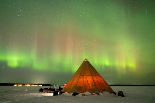 A stunning view of the Northern Lights over a tent in snowy Luleå, Sweden, beautifully captured at night.