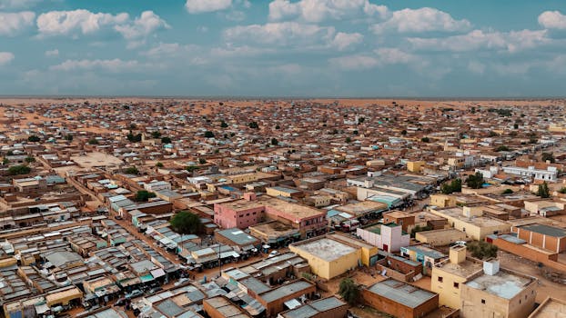Aerial panorama of a sprawling desert townscape with flat-roofed buildings under a bright sky.