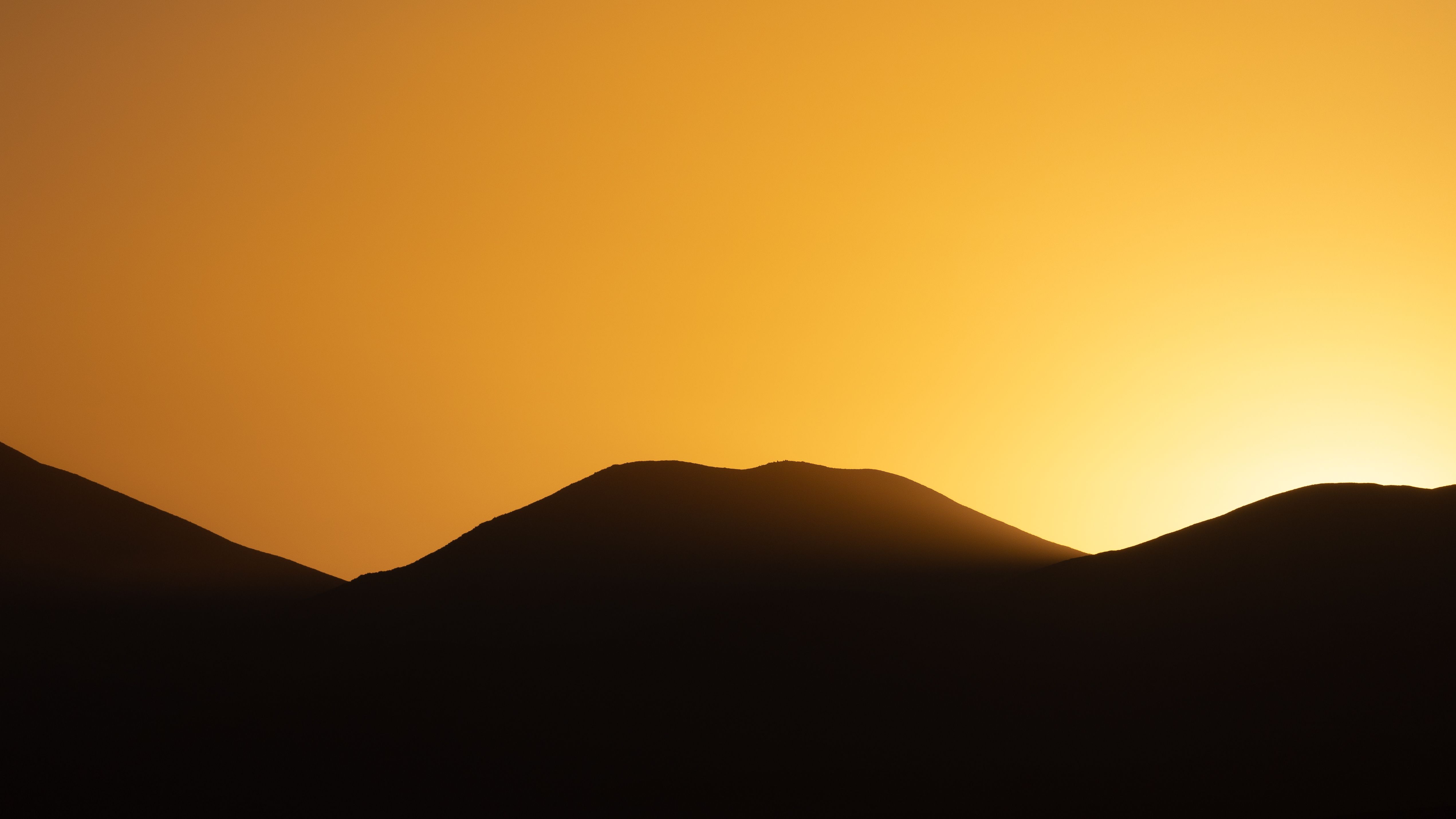 Silhouetted desert mountains at sunset with a vibrant orange sky. Silhouetted desert mountains at sunset with a vibrant orange sky.