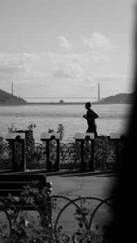 Black and white photo of a person jogging along a bridge with a serene river backdrop.