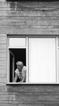Elderly woman leaning out of a window in an urban setting, pictured in black and white.
