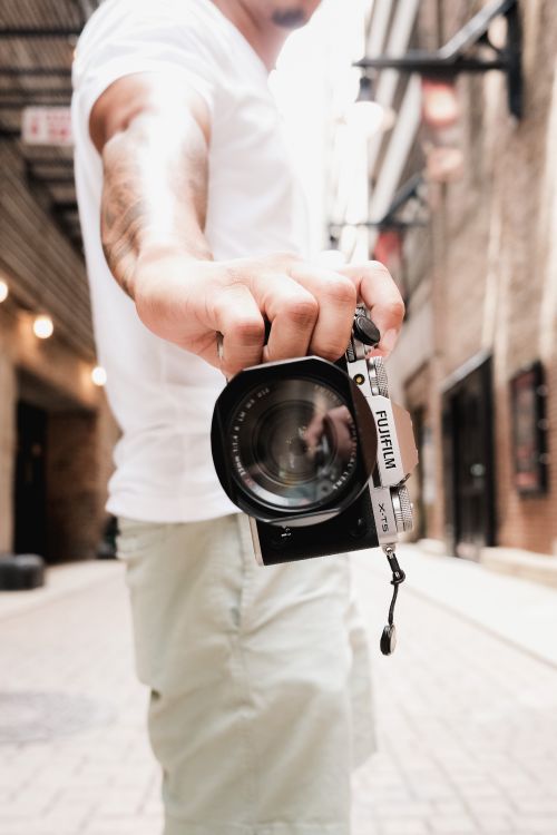 Free A young man holding a camera in a bright urban alleyway during summer. Stock Photo
