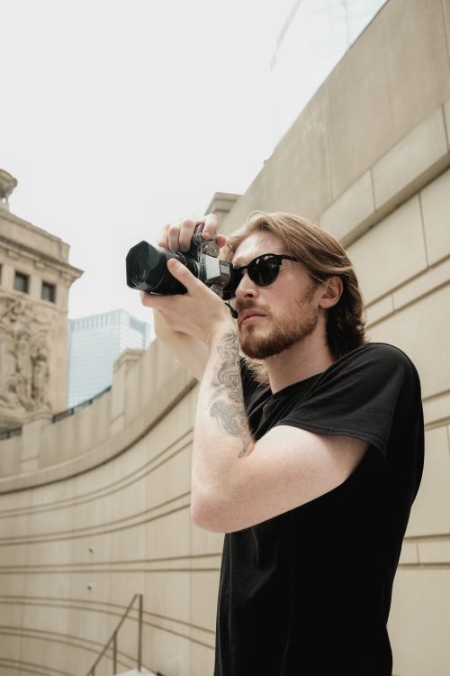 Free Young photographer with sunglasses photographing urban architecture outdoors. Stock Photo