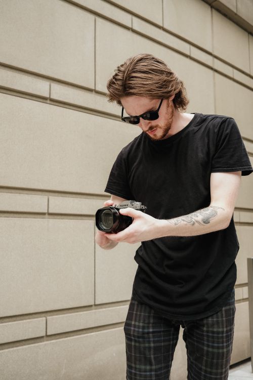 Free Portrait of a stylish male photographer examining his camera outdoors in the city. Stock Photo