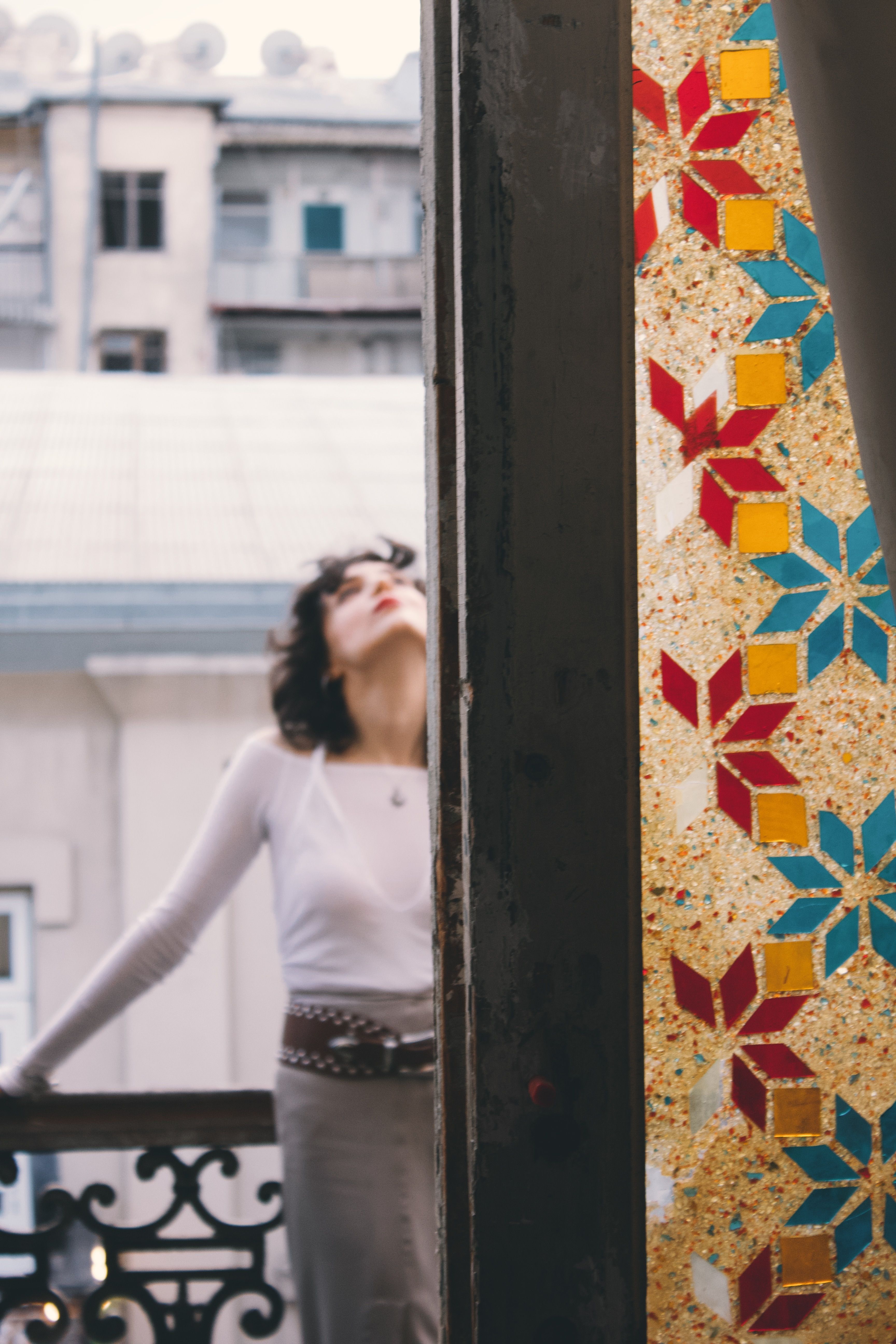 A woman enjoys a moment on a balcony next to a colorful stained glass window.