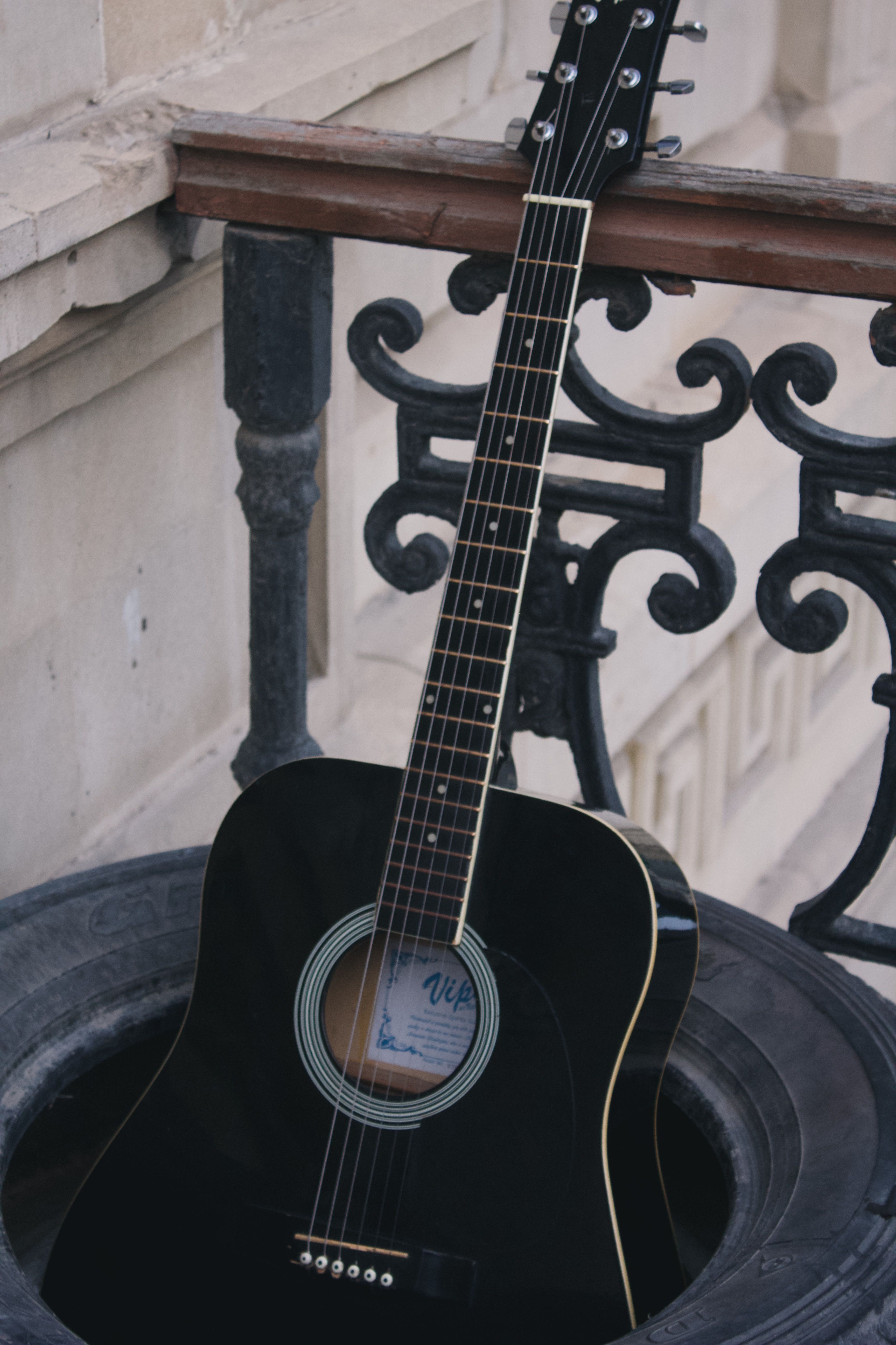 A black guitar sitting on a black railing · Free Stock Photo