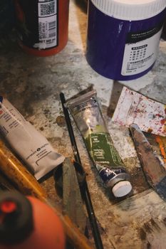 A collection of paints and brushes scattered on a well-used artist's table.