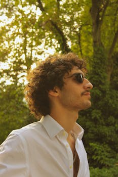 Profile shot of a young man in sunglasses and white shirt outdoors on a sunny day.