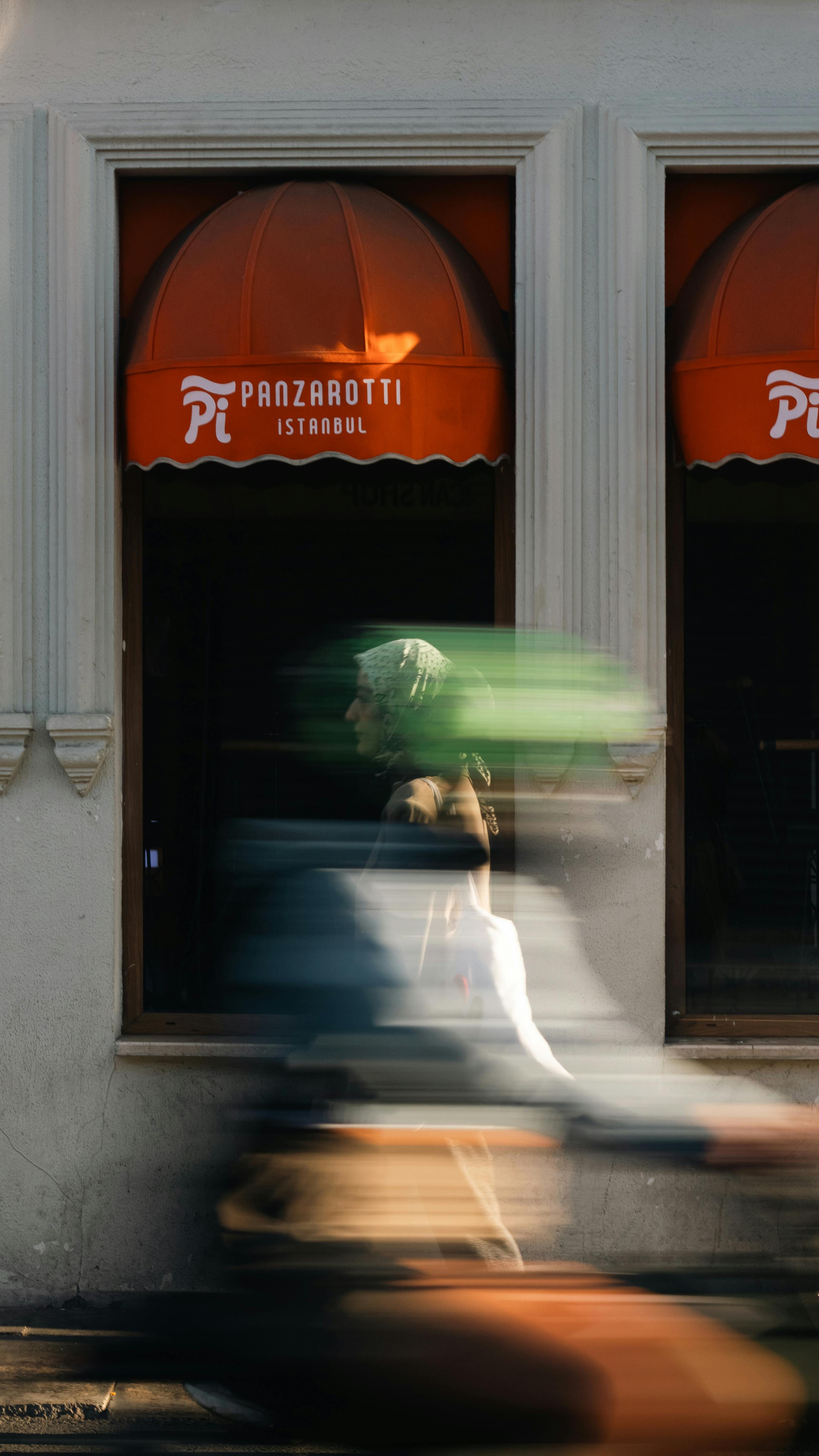 Motion blur of a person and vehicle passing a cafe in Istanbul, vibrant exterior.