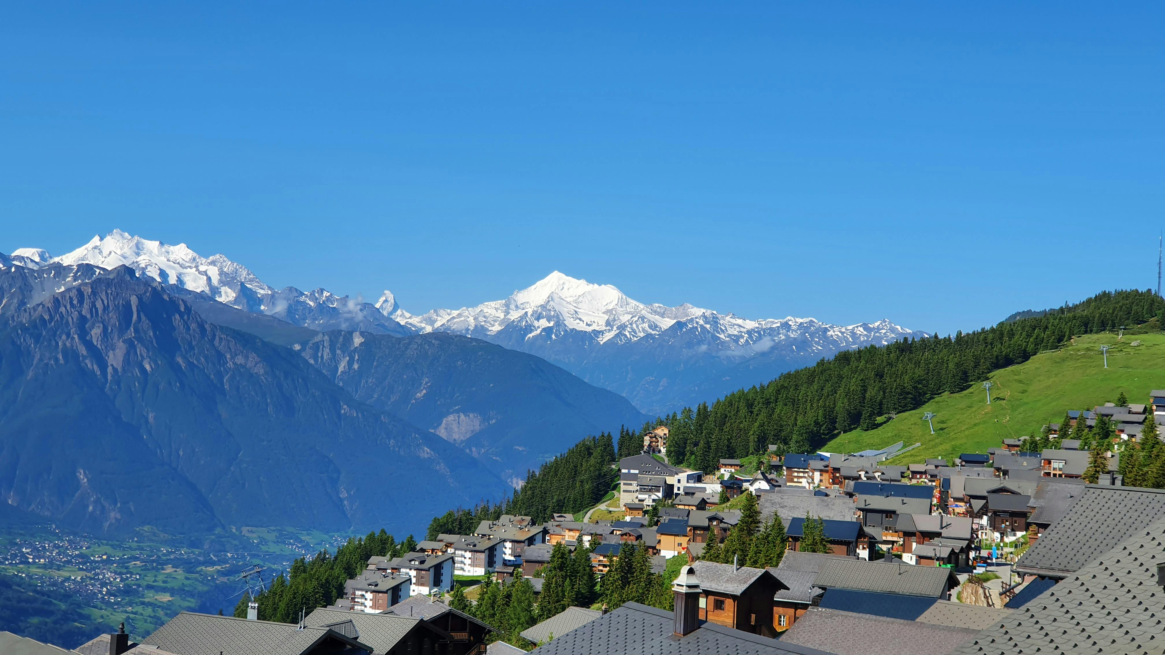 Panoramic view of Bettmeralp village with majestic Swiss Alps in the background, under a clear blue sky.