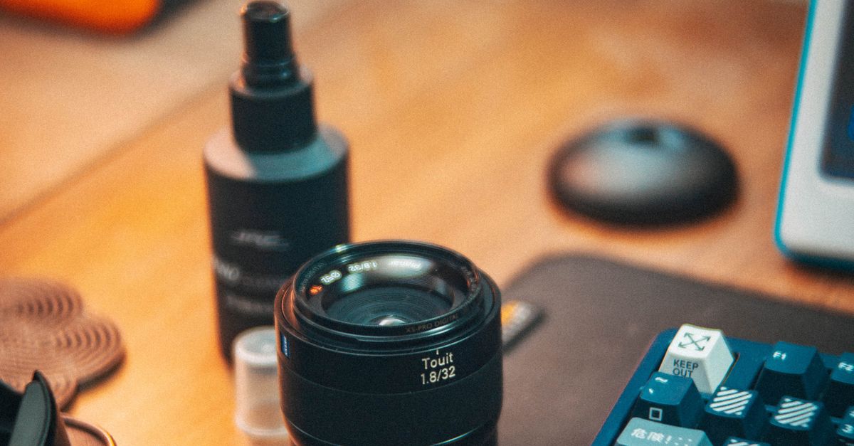 A computer monitor, camera lens and keyboard on a desk · Free Stock Photo