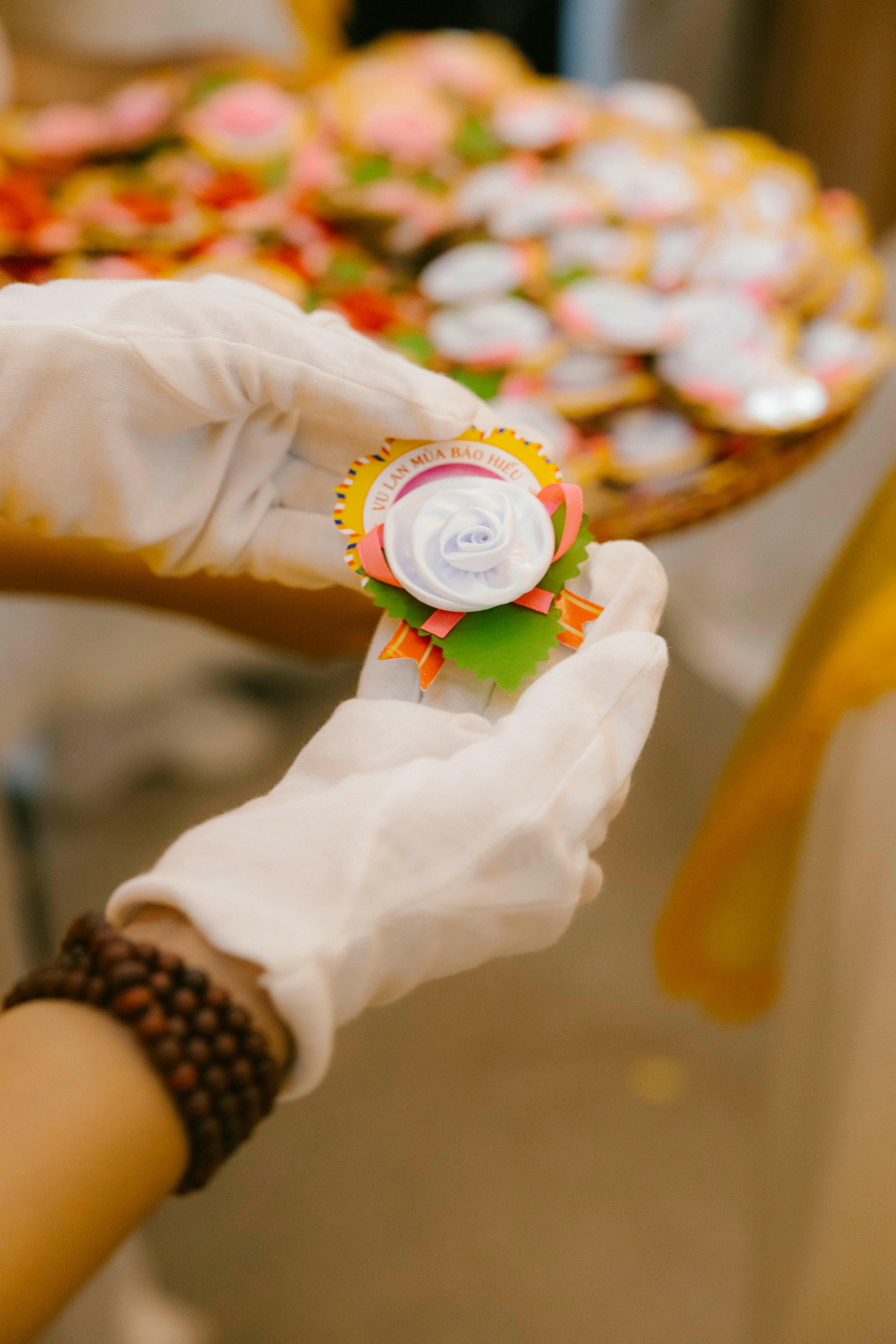 A close-up of gloved hands holding a colorful festive badge with a blurred background.