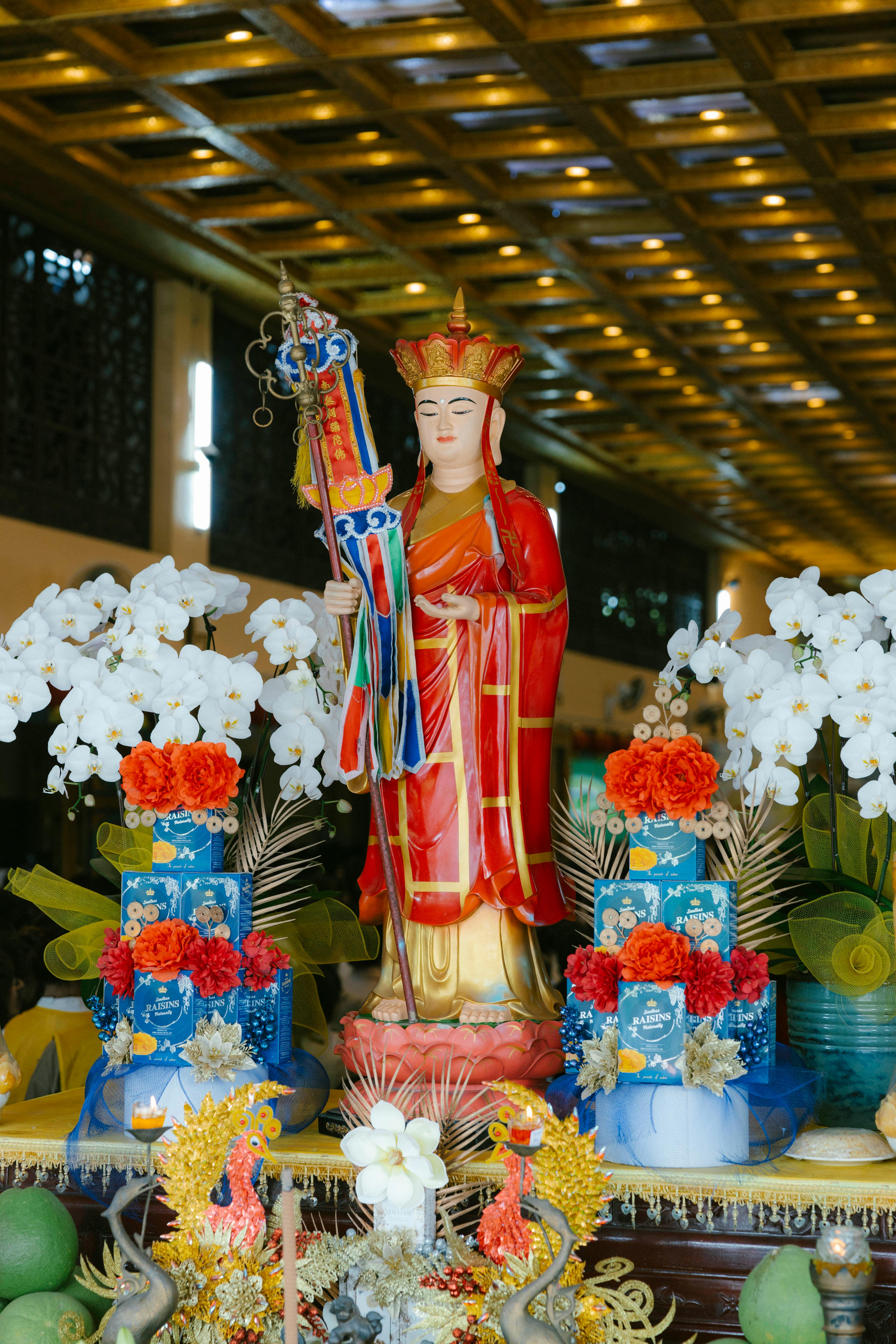 Colorful Buddhist statue with floral offerings in a serene temple setting.